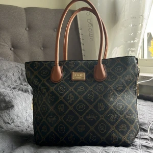 Handväska -  svart handväska med bruna handtag och guldfärgad logoplatta från L&H Firenze. Väskan har ett rutigt mönster med kedjedetaljer och olika symboler i guld. Rymligt huvudfack med dragkedja och innerficka. Perfekt för dig som gillar klassisk stil med en twist.