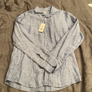 Blå linneskjorta från BRAX, M - Fräsch blå skjorta från BRAX i ren linne, modern fit. Skjortan har ett diskret mönster, klassisk krage och knappar framtill. Perfekt för dig som gillar en chill och stilren look. Storlek M, modell Harold U. Organiskt material. Köpt utomlands.