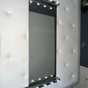 Sminkspegel med LED-lampor - Stor sminkspegel med inbyggda LED-lampor längs kanterna för optimal belysning vid sminkning eller styling. Spegeln är omgiven av en vadderad ram. Några mindre märken och slitage syns på ramen, men spegeln är i gott skick och lamporna ser hela ut.