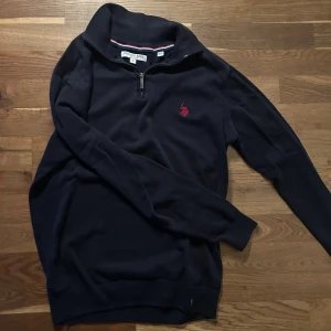 Marinblå half zip tröja U.S. Polo Assn. - Snygg marinblå långärmad tröja från U.S. Polo Assn. med röd broderad logga på bröstet. Tröjan har en half zip-dragkedja vid halsen och ribbade muddar. Gjord i mjuk bomull, perfekt för chill dagar och sköna outfits. Pris går att diskutera 