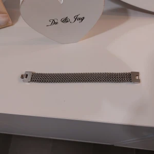 Silvrigt armband från Edblad - Snyggt och stilrent armband från Edblad i silverfärgat metall med ett flätat, zigzag-mönstrat band. Låset är robust och har Edblad-loggan ingraverad. Perfekt accessoar för dig som gillar minimalistisk design med lite edge.