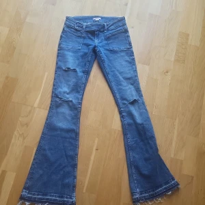 Blå bootcut jeans från Gina Tricot XS - Snygga blå bootcut jeans från Gina Tricot i storlek XS. Jeansen har slitna detaljer på benen, råa fransade benslut och stora framfickor. Tillverkade i klassiskt denimtyg med låg midja och en cool vintagekänsla.