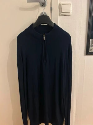 Marinblå stickad tröja med half zip - Säljer en marinblå stickad tröja från S.C.W med half zip framtill. Tröjan har lång ärm och en hög krage som kan bäras både uppvikt och nedvikt. Perfekt för dig som gillar stilrena och enkla plagg med en modern touch.