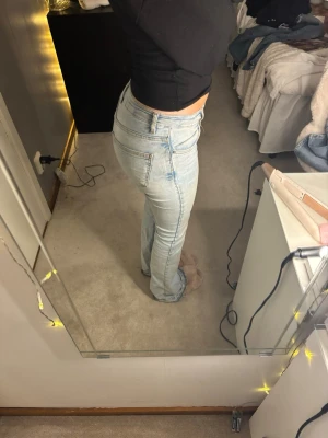 Bootcut ljusblå jeans från Perfect Jeans - Säljer ett par ljusblå bootcut jeans från Perfect Jeans i storlek 34. Jeansen har klassisk femficksdesign, hög midja och är tillverkade i mjukt denim-material. Snyggt slitna detaljer och fransad nederkant ger en chill vibe. Jeansen är lite söndriga i skrevet pågrund av att jag har själv sytt jeansen mer lågmidjade men det syns ej med jeansen på och du kan lätt sy bort hålet. Perfekt för dig som gillar retro och relaxed stil.