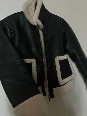 Svart fodrad skinn jacka med teddy detaljer - Säljer en svart teddy skinn jacka från Gina tricot, varm och perfekt till både höst och vinter