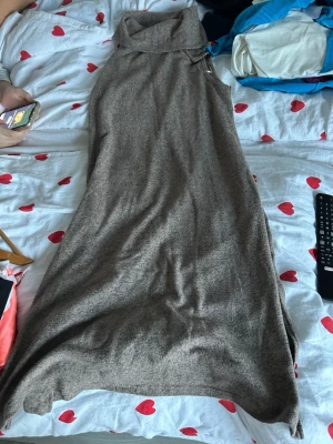 Beige långklänning från Jyothi - Säljer en beige långklänning från Jyothi i mjukt stickat material. Klänningen har en hög krage och är ärmlös, vilket ger en chill och stilren vibe. Perfekt för dig som gillar enkel design med lite extra mysfaktor.