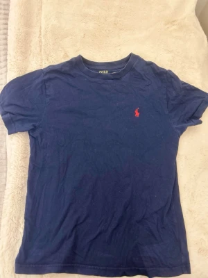 Mörkblå t-shirt från Polo Ralph Lauren -  mörkblå t-shirt från Polo Ralph Lauren med logga på bröstet. T-shirten har rund halsringning och korta ärmar. Tillverkad i mjuk bomull som känns skön mot huden. Och är i storlek S/140💕
