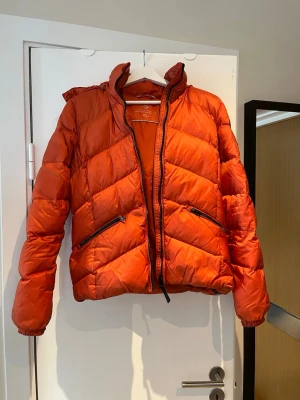 Dunjacka från Gant - Orange dunjacka från GANT. Använd men i bra skick. Finns ett litet märke på ena armen, se bild. Storlek Small (160/80A)