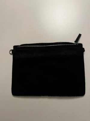 Svart axelväska från Carin Wester - Snygg svart axelväska från Carin Wester i pälsimitation på ena sidan och slät skinnkänsla på andra. Väskan har avtagbar axelrem. Kommer med dustbag. Pris går att diskutera.