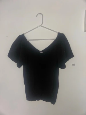 Svart ribbad topp från ONLY - Säljer en svart ribbad topp från ONLY med v-ringad hals och korta ärmar. Toppen har en slim passform och är tillverkad i mjukt, stretchigt material som sitter snyggt på kroppen. Perfekt för dig som gillar stilrena och enkla plagg.