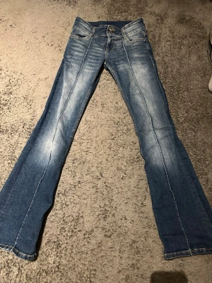 Blå bootcut jeans från Bershka  - Snygga blå jeans med bootcut passform och coola slitningar. Snygga fickor och även två knappar framtill. Jeansen har en lätt tvättad look och är gjorda i mjukt denim-material som sitter skönt hela dagen.
