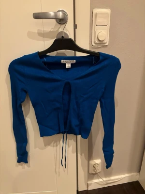 Blå ribbad kofta från Amisu - Säljer en blå ribbad kofta från Amisu i storlek S. Koftan har v-ringning, långa ärmar och snörning framtill som ger en croppad look. Perfekt för dig som vill ha en trendig och enkel tröja att styla till olika outfits.