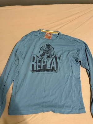 Stilig tröja - REPLAY  (tshirt t-shirt tröja) - Säljer en blå långärmad topp från Replay med stort tryck framtill och coolt motiv. Toppen har rund hals och är gjord i mjuk bomull, perfekt för en chill och avslappnad stil. Passar dig som gillar streetwear och vill ha något med lite edge.