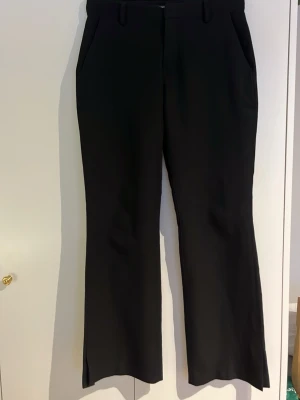 Svarta kostymbyxor BikBok - Säljer ett par svarta kostymbyxor från BikBok i storlek 36. Byxorna har bootcut-modell med slits nertill, bälteshällor och fickor fram. Snygg passform och klassisk look, perfekta till en clean outfit. Modellen är Vera och byxorna är uppsydda för att passa någon som är ca 160 cm