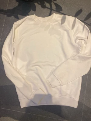 Vit sweatshirt från Peak Performance - Säljer en stilren vit sweatshirt från Peak Performance med diskret logga på bröstet. Tröjan har rund hals, långa ärmar och ribbade muddar vid ärmslut och nederkant. Perfekt för dig som gillar enkel och clean stil.