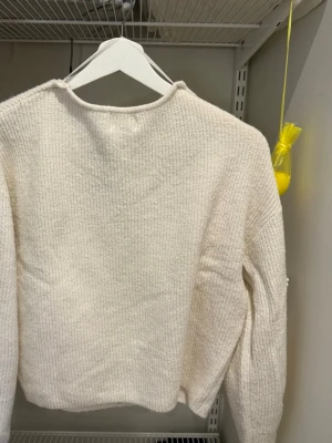 Vit stickad v-ringad tröja - Mysig vit stickad tröja med v-ringning och lång ärm. Tröjan har en enkel, ribbad struktur och en något croppad passform som ger en avslappnad vibe. Perfekt för lager på lager under kyliga dagar.