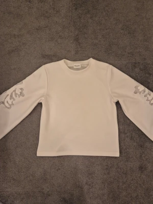 Vit tröja med spetsdetaljer  - Supersnygg vit tröja från Kappahl i storlek XS. Tröjan har långa ärmar och coola spetsdetaljer i form av broderade mönster på båda ärmarna. Perfekt för dig som vill ha något enkelt men ändå med en twist. Väldigt skönt material. Hör av er om ni har några frågor🤞
