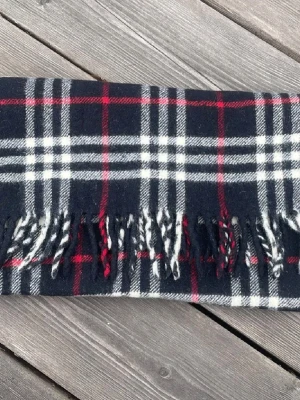 Burberry halsduk - Asfet halsduk från Burberry i 100% kashmir med klassiskt rutigt mönster i svart, vitt och rött. Den är i prinicip i nyskick med inga defekter och halsduken är extremt mjuk och len. Givetvis äkta, skriv om du har några frågor