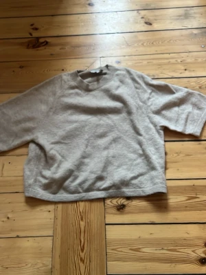 Beige tröja från & Other Stories - Beige, mjuk och lite boxig tröja från & Other Stories. Tröjan har rund halsringning, kortare ärmar och är tillverkad i ett stickat material som känns riktigt skönt mot huden. Perfekt för lager-på-lager och enkel att matcha med det mesta.