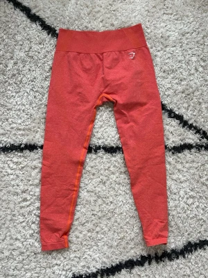 Seamless tights från Gymshark - Snygga leggings från Gymshark med hög midja och diskret mönster. Stretchigt material som sitter tight och bekvämt, perfekt för träning. Gymshark-logga i vitt på höften och benet. Superskön passform och cool färg, korall, orange/röd. Storlekslappen är avklippt men de är storlek M <3