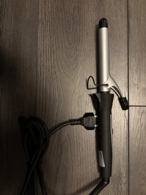 Svart och silver locktång - En stilren locktång i svart och silver med ergonomiskt handtag och klassisk klämma. Utrustad med lång sladd och EU-kontakt. Perfekt för att skapa snygga lockar och vågor i håret. Tillverkad i metall och plast.