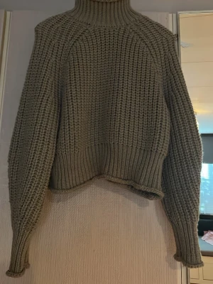 Olivgrön stickad jumper - Säljer en chunky olivgrön stickad jumper med bred ribbad mudd i hals, ärmslut och nederkant. Tröjan har en boxy, croppad passform och långa ärmar. Perfekt för lager på lager och riktigt mysig till hösten.