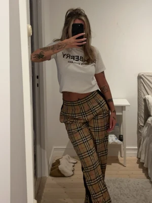 Rutiga byxor från Burberry - Snygga chinos i klassiskt beige rutigt mönster från Burberry. Byxorna har svarta sidopaneler och rak passform.