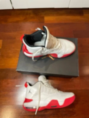 Vita och röda Air Jordan sneakers - Snygga Air Jordan sneakers i vitt och rött med svart detalj och klassisk Jumpman-logga på sidan. Skorna har en låg silhuett, vadderad plös och sula med bra grepp. Perfekta för dig som gillar streetwear och sportig stil.
