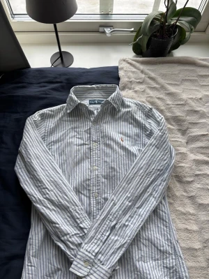 Polo Ralph lauren skjorta  - Säljer en riktig skön vit blå randig  Ralph lauren skjora. Använd några fåtal gånger i somras,  så det är fint skick.         MStorlek M/L👍🏼       Skick 8/10🤩    Vid funderingar så är de bara att höra av sig! Priset är diskuterbart!