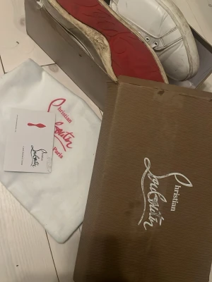 Vita Christian Louboutin sneakers - Snygga vita sneakers från Christian Louboutin med klassisk röd sula och vita skosnören. Skorna är låga och tillverkade i läder, med diskreta sömdetaljer och metallfärgade öljetter. Kommer med originalkartong, dustbag och äkthetskort.