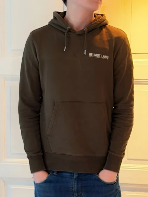 Olivgrön hoodie från Helmut Lang - (Moddelen är 184 och väger 75) Snygg olivgrön hoodie från Helmut Lang med klassisk känguruficka och dragsko i huvan. Mjuk bomullskänsla och diskret logga på bröstet. Perfekt för en avslappnad och trendig stil.