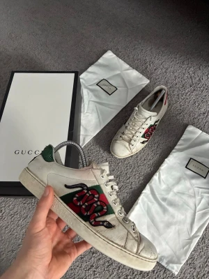 Gucci Ace skor - Gucci Ace sneakers i vitt läder med broderad röd och svart orm på sidan, gröna Skorna är använda men ändå i bra skick. Levereras med originalkartong och dustbag. Hör av er vid frågor!