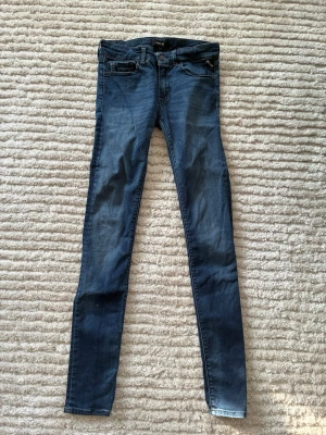Blå skinny jeans från Replay - Säljer ett par blå skinny jeans från Replay med klassisk femficksdesign och dragkedjegylf. Jeansen har en snygg tvättad look och smal passform som sitter tight längs benen. Perfekta till sneakers eller boots för en avslappnad stil. Storlek 27/32