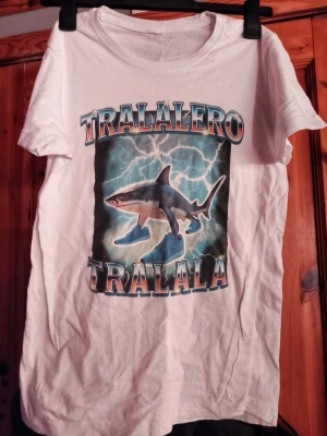Tralalero tralala t shirt - Det är en t shirt med motivet tralalero tralala på inköpt sommaren 2025, står ingen storlek i den men dom på butiken sa medium men jag skulle säga att den är nånstans mellan medium och small Kan tänka mig att gå ner i pris om de skulle vara så