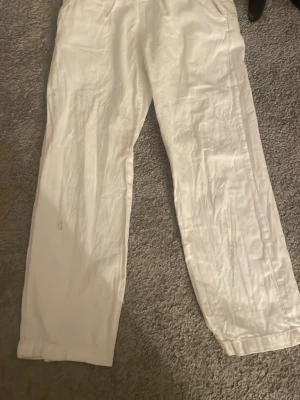 Vita linnebyxor från Kappahl - Säljer ett par vita linnebyxor från Kappahl med avslappnad passform och resår i midjan samt dragsko. Byxorna har raka ben och är tillverkade i ett lätt och luftigt linnematerial, perfekta för en chill och stilren look.Den här lite bränn märken vid midjan men man ser knappt dem så annars funkar det! 