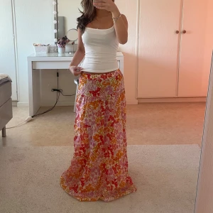 Blommig långkjol i rosa och orange - Jättefin långkjol med blommigt mönster i rosa, orange och vitt. Den är lätt och luftig helt perfekt  under sommartider. passform, perfekt för varmare dagar. Ett skönt material och midjebandet är stretchigt. Använd en enstaka gång så den är som ny! Passar både xs och s.