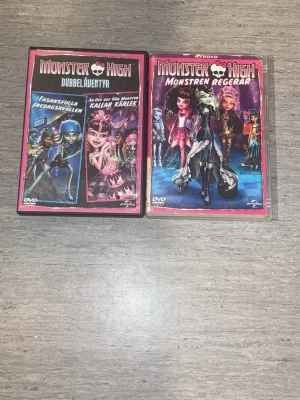 Monster High DVD-filmer - Två DVD-filmer från Monster High: 'Dubbeläventyr' och 'Monstren Regerar'. Omslagen är färgglada med karaktärer från Monster High-serien. Perfekt för dig som gillar animerade äventyr och coola monster. Båda filmerna är på svenska och har snygga rosa och svarta fodral. Förekommer repor på skivan och ena fodralet lite förstört men inget som påverkar!.