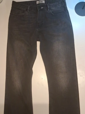 Svarta raka jeans från Acne - Säljer ett par svarta jeans från Acne med rak passform och klassisk femficksdesign. Jeansen har en snygg tvättad look och är tillverkade i kraftigt denimtyg. Perfekta för dig som gillar stilrena och tidlösa plagg.