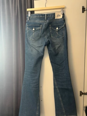 Blå bootcut jeans med slitningar från Gina Tricot  - Jag säljer ett par bootcut jeans, jag säljer det eftersom det aldrig kommer till användning och ligger bara i garderoben. De är Snygga blå bootcut jeans från gina tricot med slitna detaljer framtill och klassiska bakfickor med lock och vita knappar. Jeansen har en lätt utsvängd passform och är tillverkade i denim med en cool tvättad look.