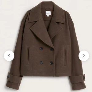 Brun ullkappa från Lindex  - Kort brun kappa i ullmix från Lindex  med dubbelknäppning, bred krage och raka ärmar med dekorativa knappar vid ärmslut. Två fickor framtill och stilren, snygg passform. Perfekt för kyliga dagar. Använd förra vår/höst så något nopprig🩷 Annars helt perfekt skick💕Orginalpris 899 säljer för 400💗 prutbart!