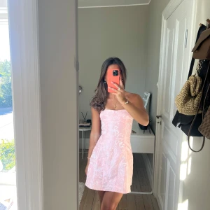 Ljusrosa axelbandslös kortklänning - Superfin ljusrosa kortklänning i mjuk sammet med axelbandslös design och snörning i ryggen. Klänningen har en lätt A-linjeformad siluett och ger en romantisk vibe med sitt skimrande material. Perfekt för dig som vill sticka ut med en söt och trendig look. Storlek 34 men lite liten i storleken 