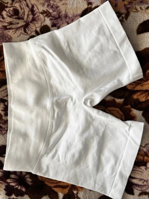 Vita seamless DFYNE  - Säljer ett par vita seamless cykelshorts från DFYNE. De är tillverkade i ett stretchigt och mjukt material som sitter skönt mot kroppen. Perfekta för träning eller som basplagg under kjol eller klänning. Midjan är bred och elastisk för extra komfort.