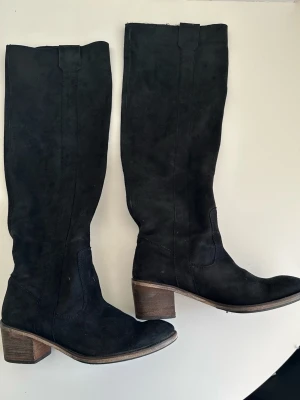 Svarta knähöga stövlar i äkta mocka - Klassiska svarta knähöga stövlar i äkta skinn / läder / mocka från EXIT i storlek 39. Supermjuka och sköna. Mycket gott skick!!  Hämtas i Stockholm eller skickas mot porto.