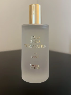 Zara Red Temptation Hair Mist - Zara Red Temptation Hair Mist i en frostad glasflaska med guldfärgad kork och text. Doftmisten är elegant och stilren, perfekt för att fräscha upp håret med en lyxig känsla. Flaskan har en modern, cylindrisk form och exklusiv design.