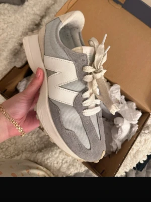 Gråa New Balance sneakers med mockadetaljer - Snygga sneakers från New Balance i grått och vitt med stora N-loggan på sidan. Skorna har en mix av mocka och mesh, chunky sula och klassiska snörningar. Perfekta för en trendig streetstyle-look.