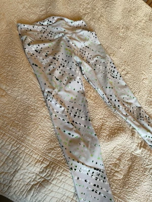 Vita träningsleggings med mönster - Säljer ett par mönstrade träningstights med svart och grönt abstrakt mönster på vit bakgrund. De är väldigt sköna i midjan. Perfekta för gymmet eller löpning. Materialet är stretchigt och följsamt för maximal rörelsefrihet. Jag är 160 cm lång och de går till vad/vristerna på mig. Saknar tyvärr lapp med märke/materialanvisning. 