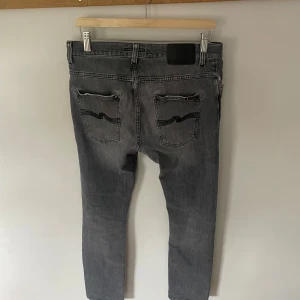 Grå Nudie Jeans Grim Tim  - Säljer nu mina gråa nudie jeans i modellen grim tim. Storlek 32/32. Bra skick men finns lite lagningar på jeansen, se bilderna.