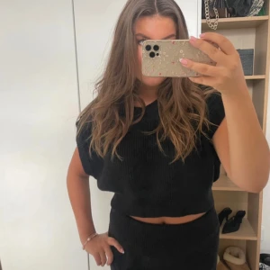 Svart väst/topp från Zara - Svart stickad topp från Zara med korta ärmar och rund hals. Modellen är croppad upptill och har en ribbad struktur som ger en snygg och modern look. Perfekt för dig som gillar en enkel men trendig stil.