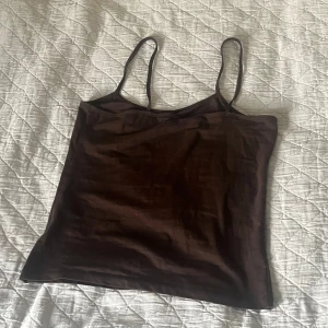 Brun linnetopp från Åhléns  - Snygg brun linnetopp från Åhléns med smala axelband och rak passform. Toppen är ärmlös och har en enkel, stilren design som är lätt att matcha med olika outfits. Perfekt för dig som gillar minimalistisk stil och jordnära färger.