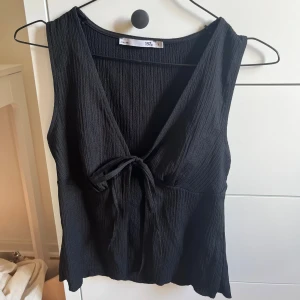 Svart linnetopp med knyte  - Svart linnetopp med djup v-ringning och knyt framtill. 